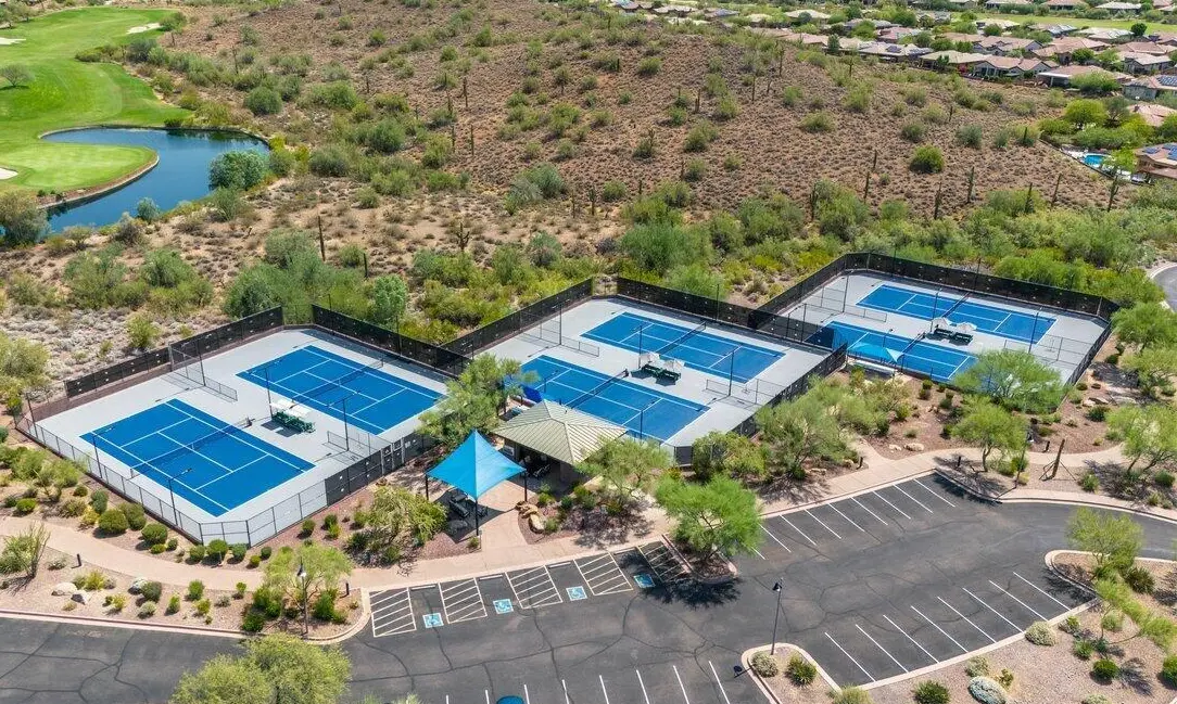 A neatly trimmed front yard in the Palm Springs style features a rectangular patch of vibrant green artificial grass edged with wooden borders. Surrounding areas have white gravel with sparse, neatly arranged plants, contributing to a modern and minimalist landscape design by Coachella Valley Turf.